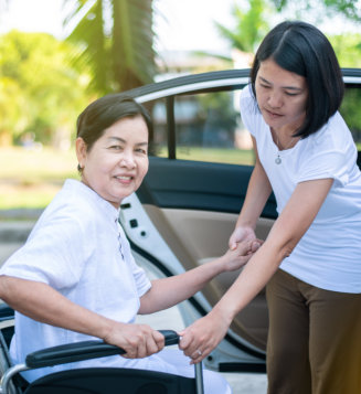  Caregiver helping senior handicapped women from wheelchair get into car