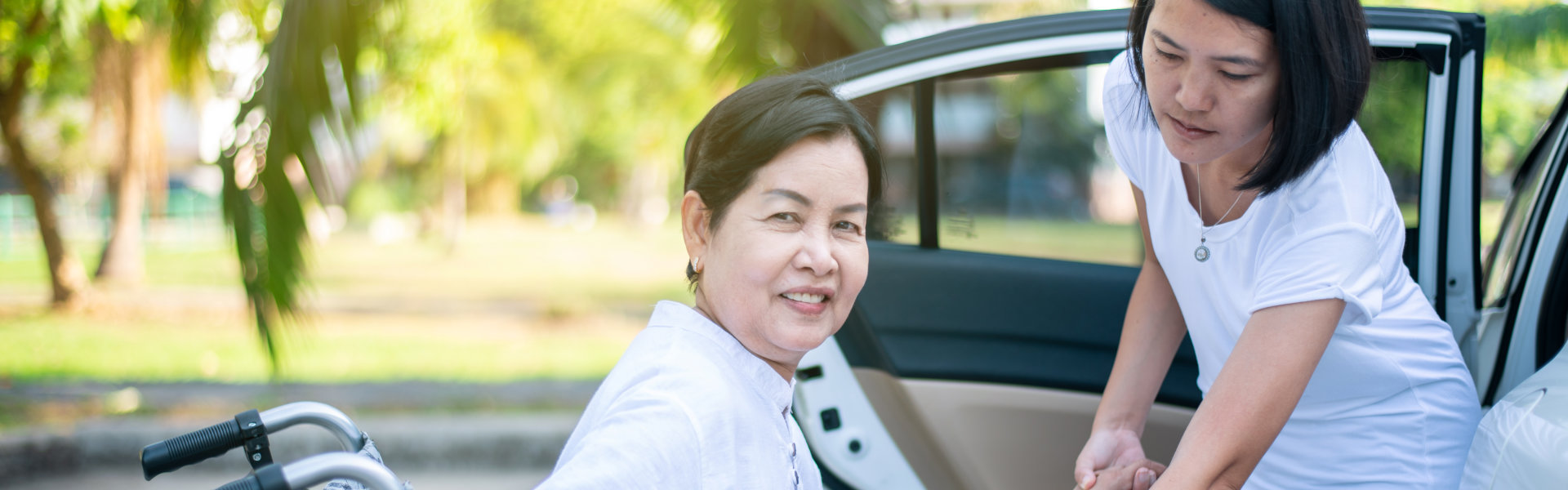 Caregiver helping senior handicapped women from wheelchair get into car